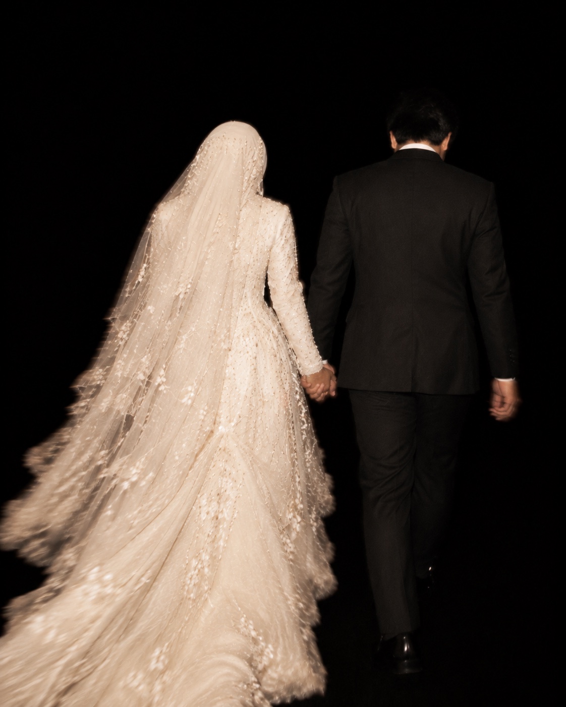 Ilustrasi AI: Pasangan pengantin dari belakang dengan gaun putih berhijab dan jas hitam diterangi flash