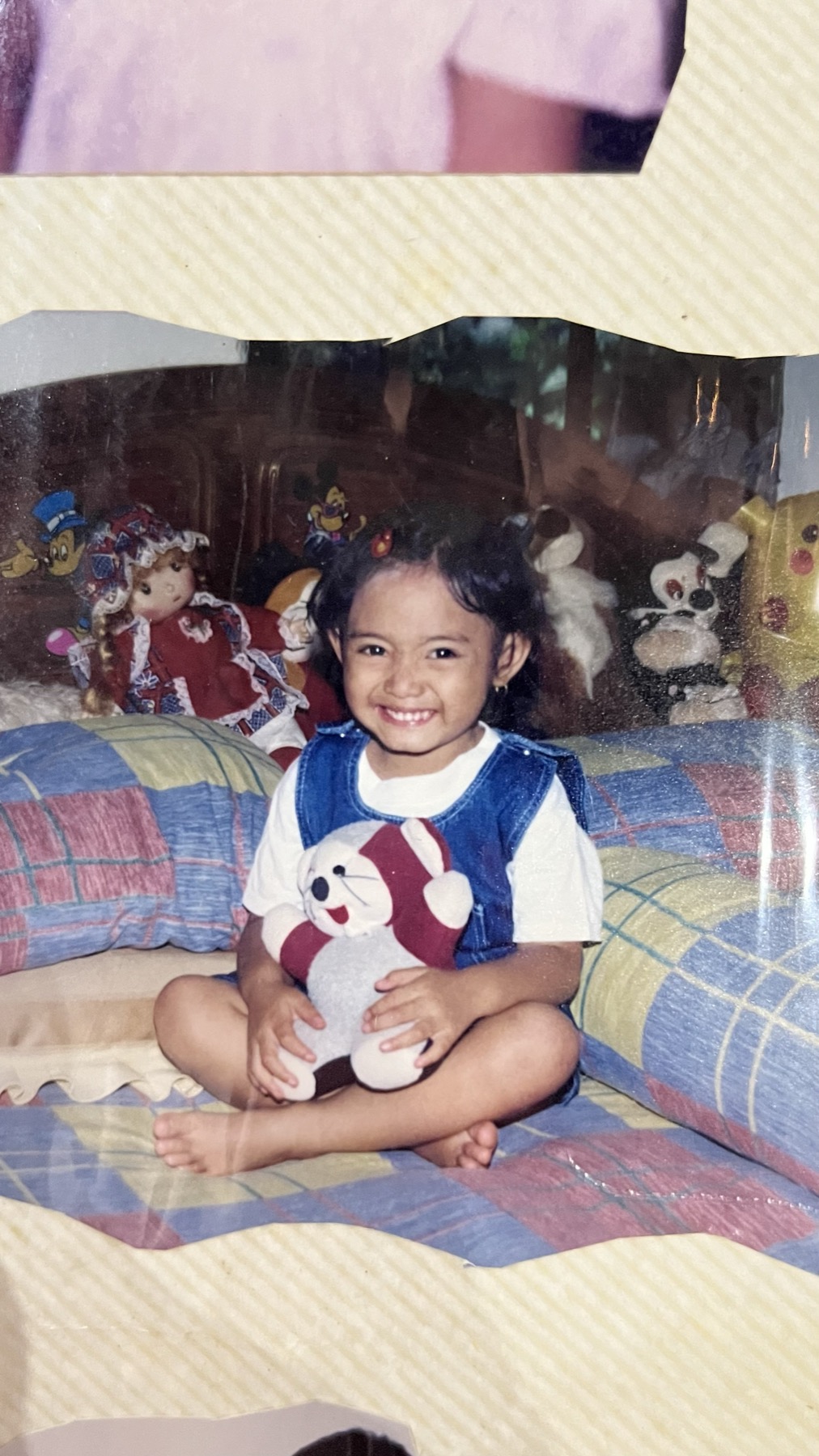 Foto masa kecil Lia sedang tersenyum sambil memegang boneka